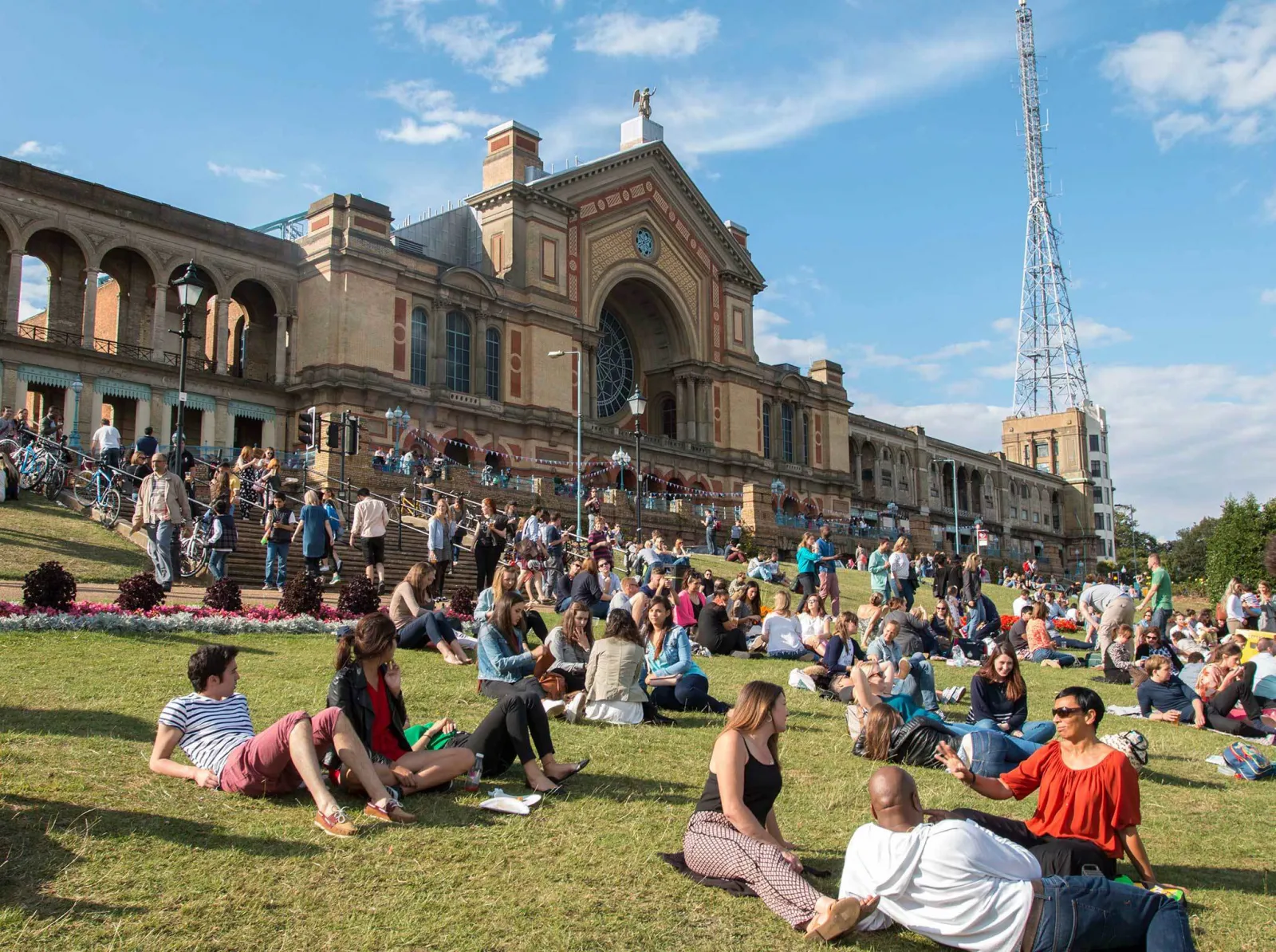 People sitting out on the grass in front of Alexandra Palace on a sunny afternoon